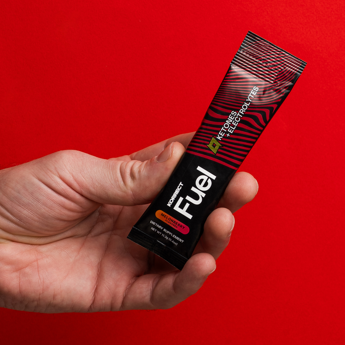 A hand holding a Korrect Fuel stick packet against red