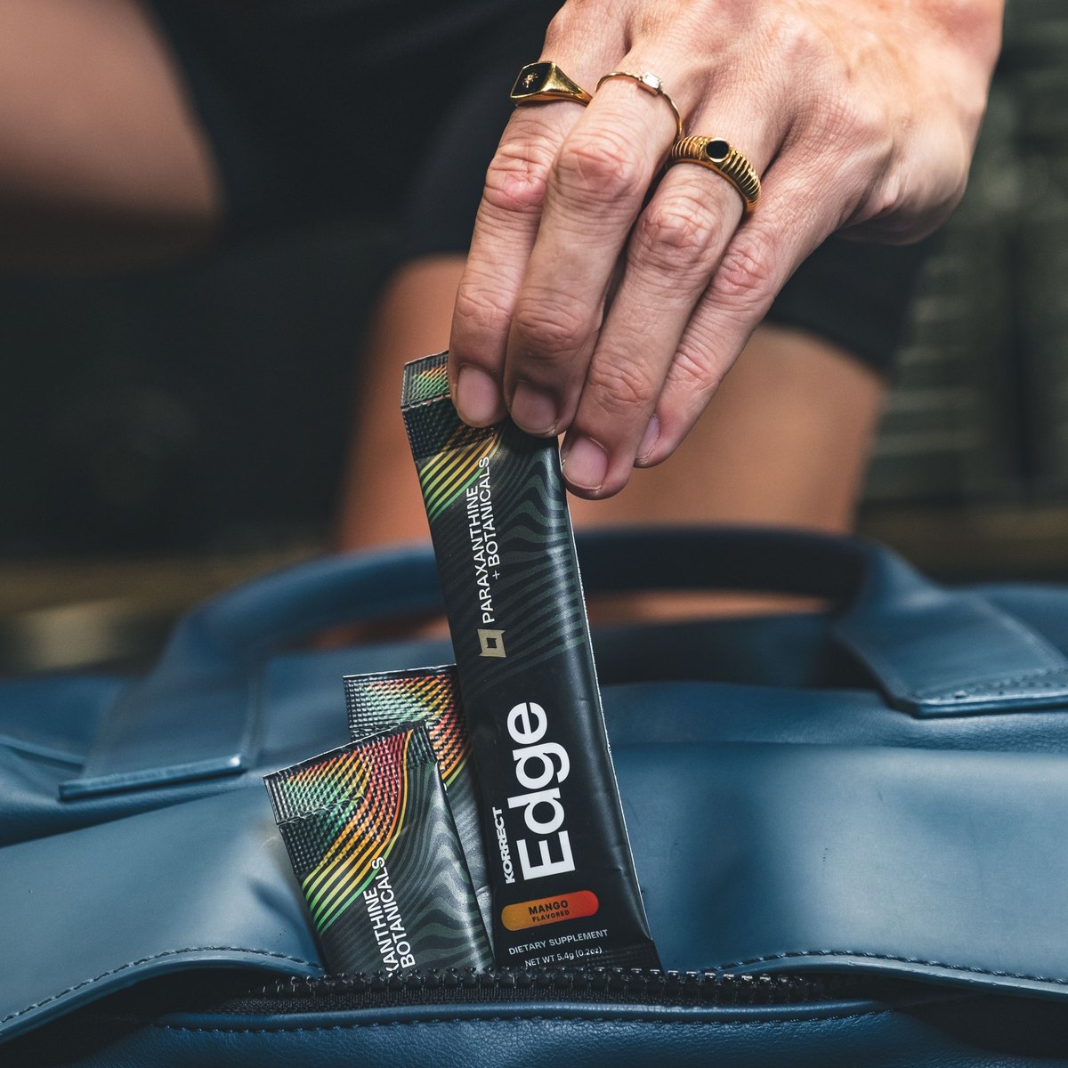 A hand pulling a Korrect Edge Instant stick packet out of a gym bag, two more packets beside it